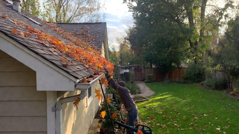 early fall home maintenance checklist — A cozy suburban home in early fall with colorful leaves on the ground, a homeowner wearing gloves cleaning gutters, and garden tools nearby, suggesting active seasonal maintenance.
